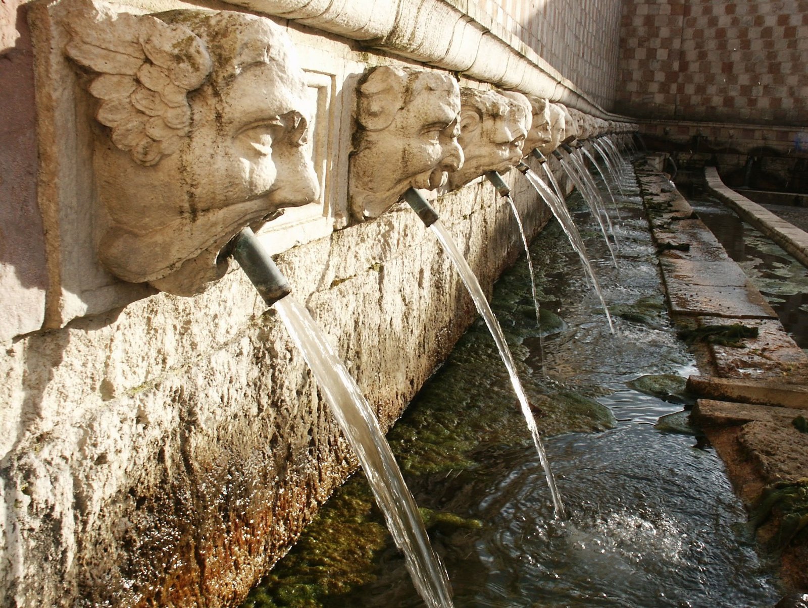 Stone faces pouring water into a historic fountain in Abruzzo