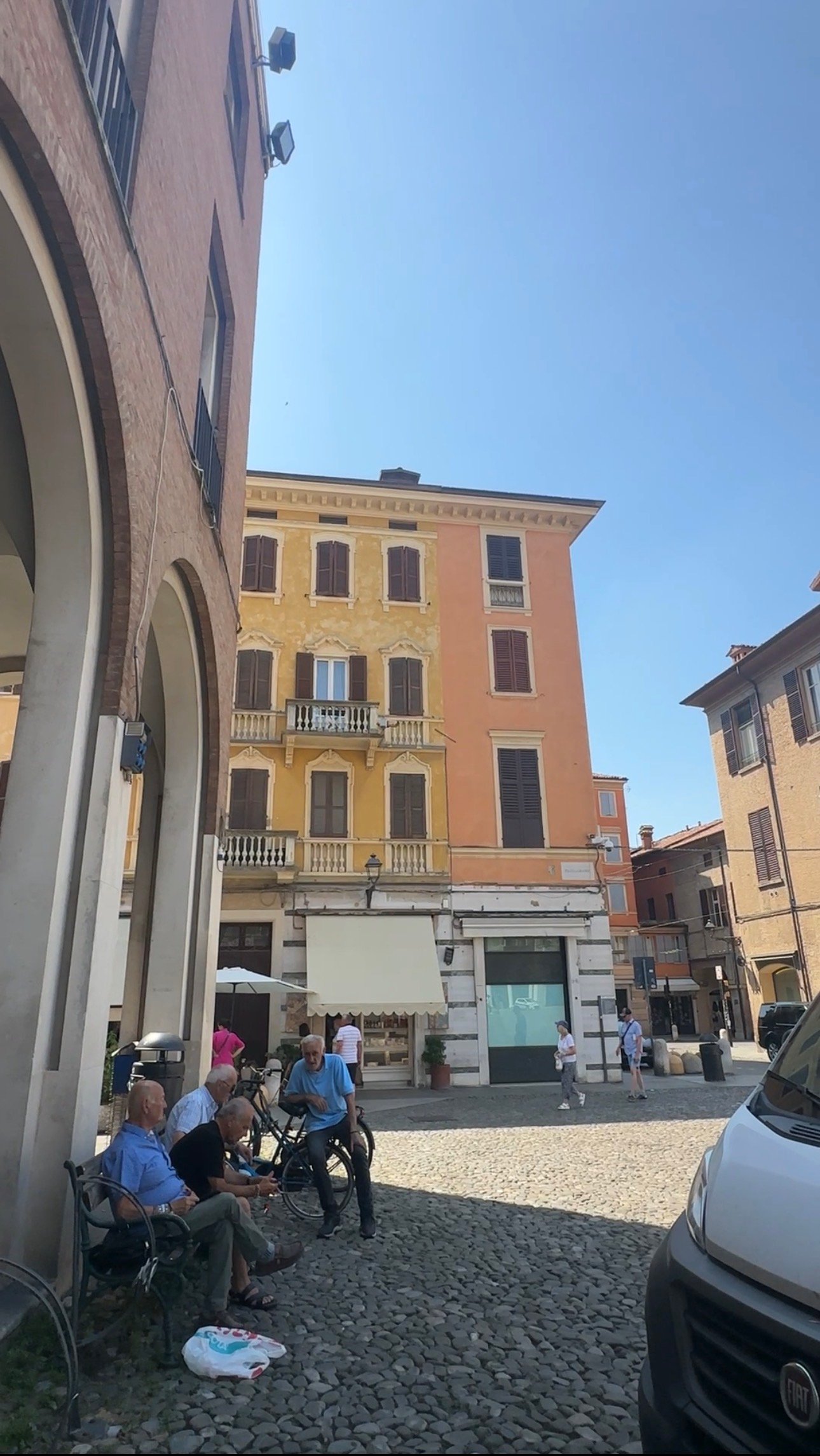 Men chatting beside a bench and bicycles in a Modena piazza