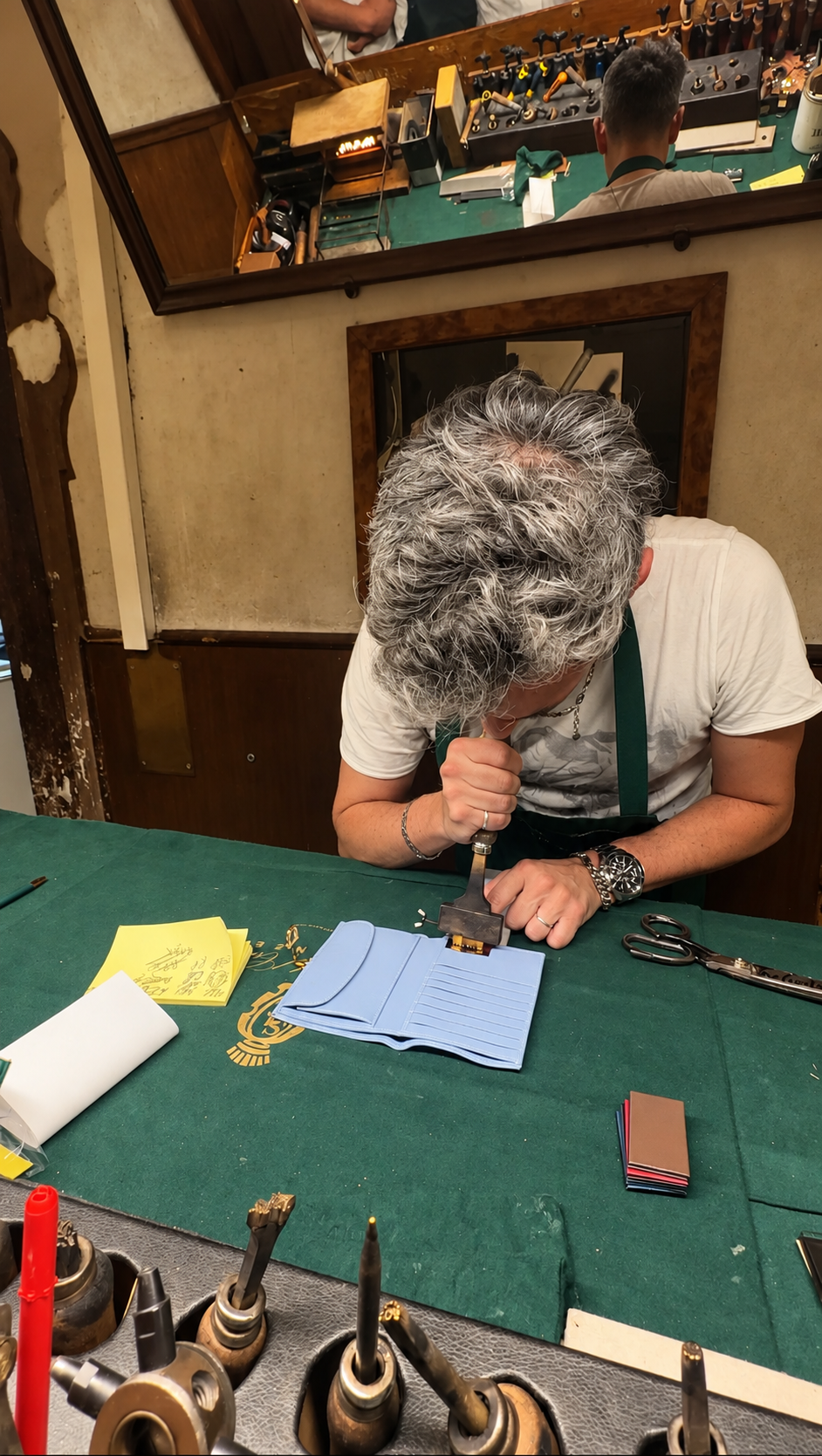 A Florence leather craftsman working on a pale blue leather piece at a green workbench