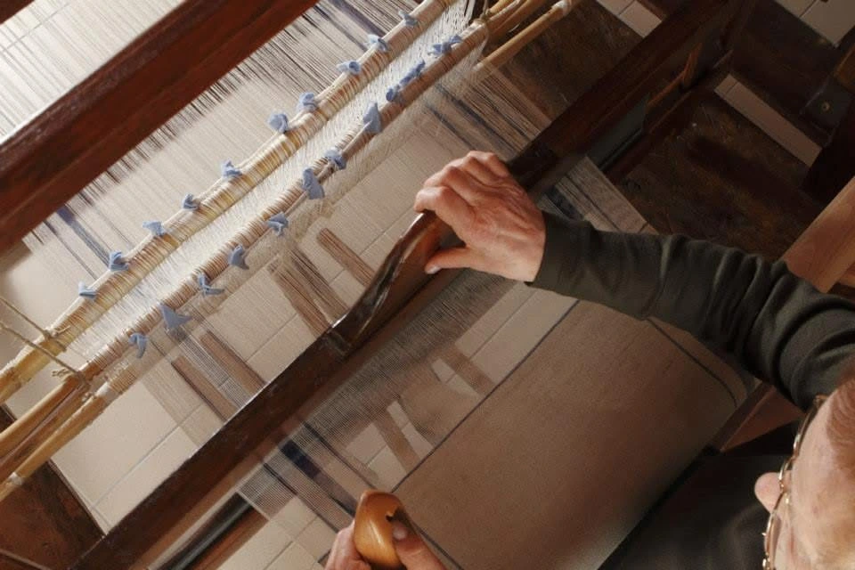 Hands guiding threads on a wooden loom in Casoli