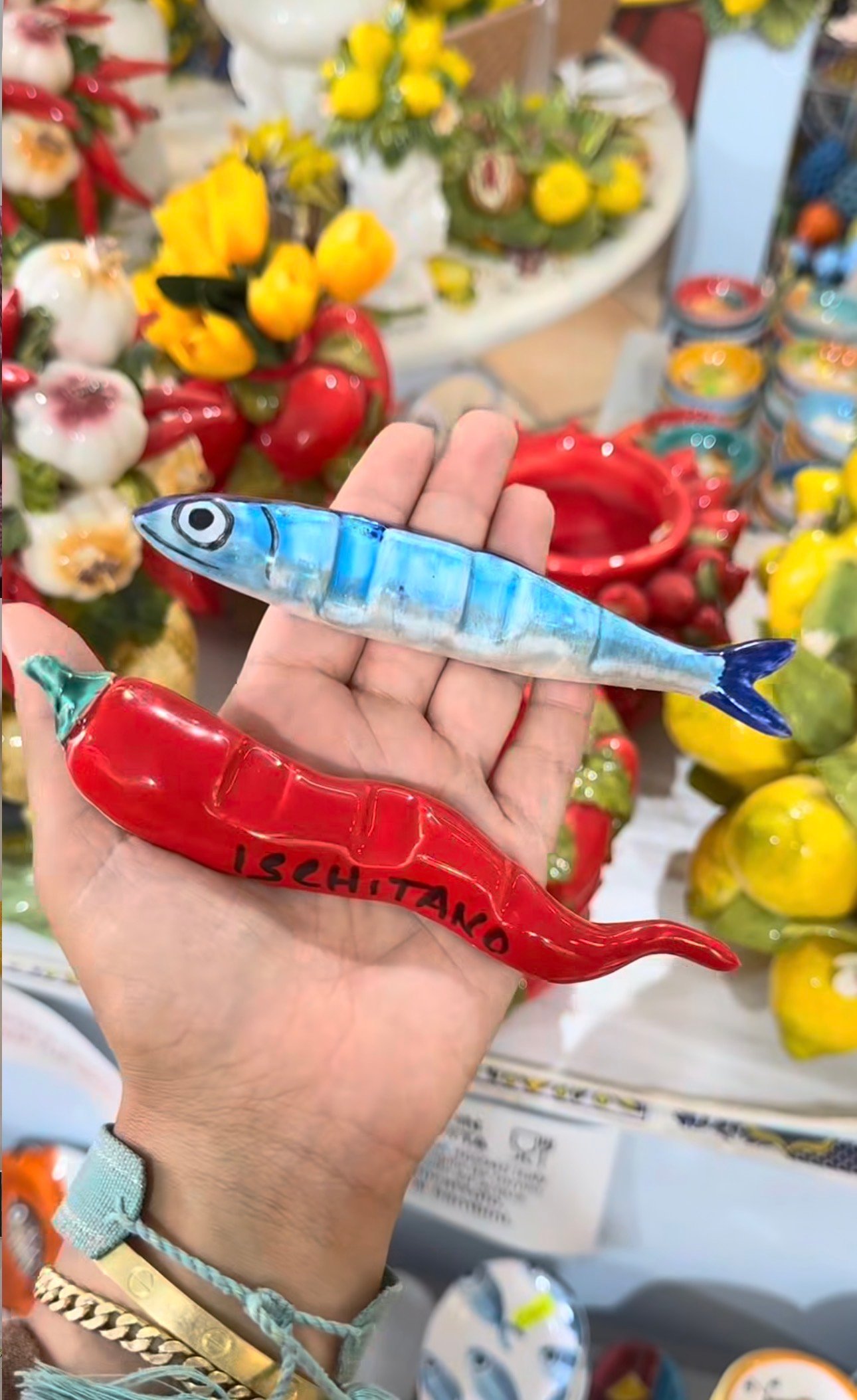 A hand holding a blue ceramic fish and a red Ischitano pepper among colorful island ceramics