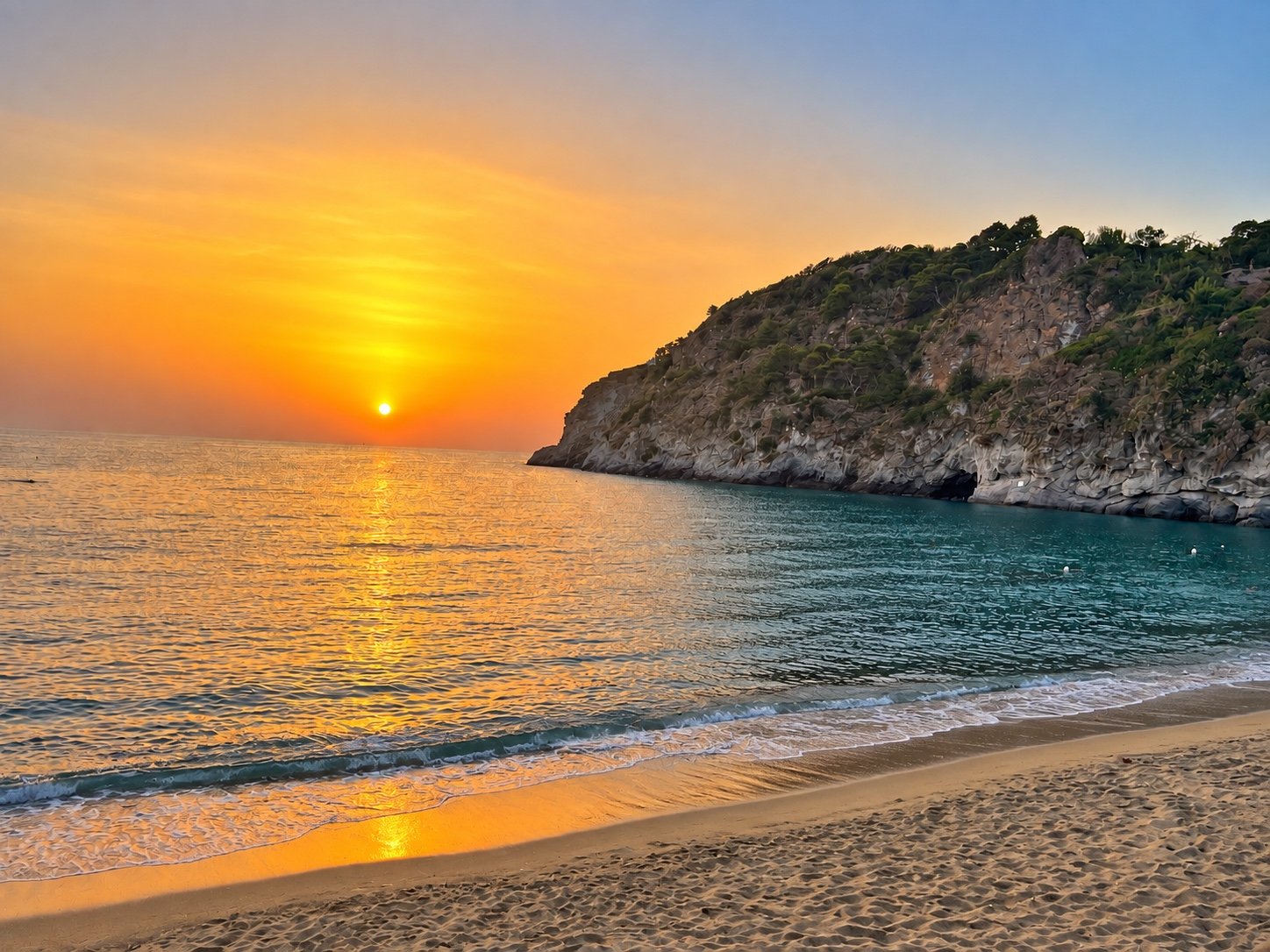 Sunset over a quiet Ischia beach with a rocky headland beside the sea