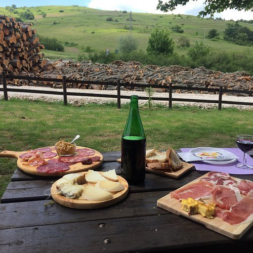 Homemade wine in a reused green bottle beside boards of meats, cheese and bread on an outdoor country table