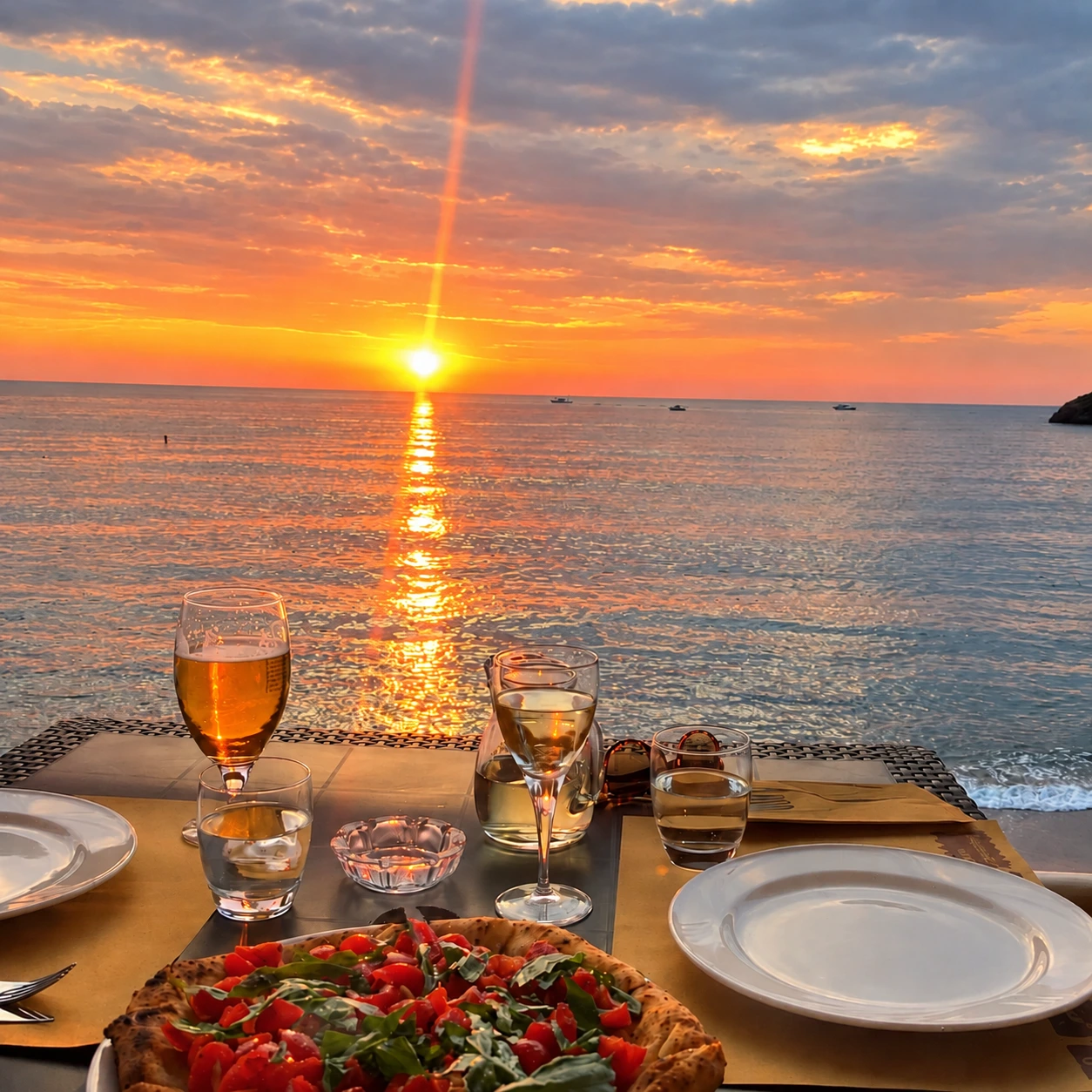 Pizza and glasses on a dinner table overlooking the sea at sunset