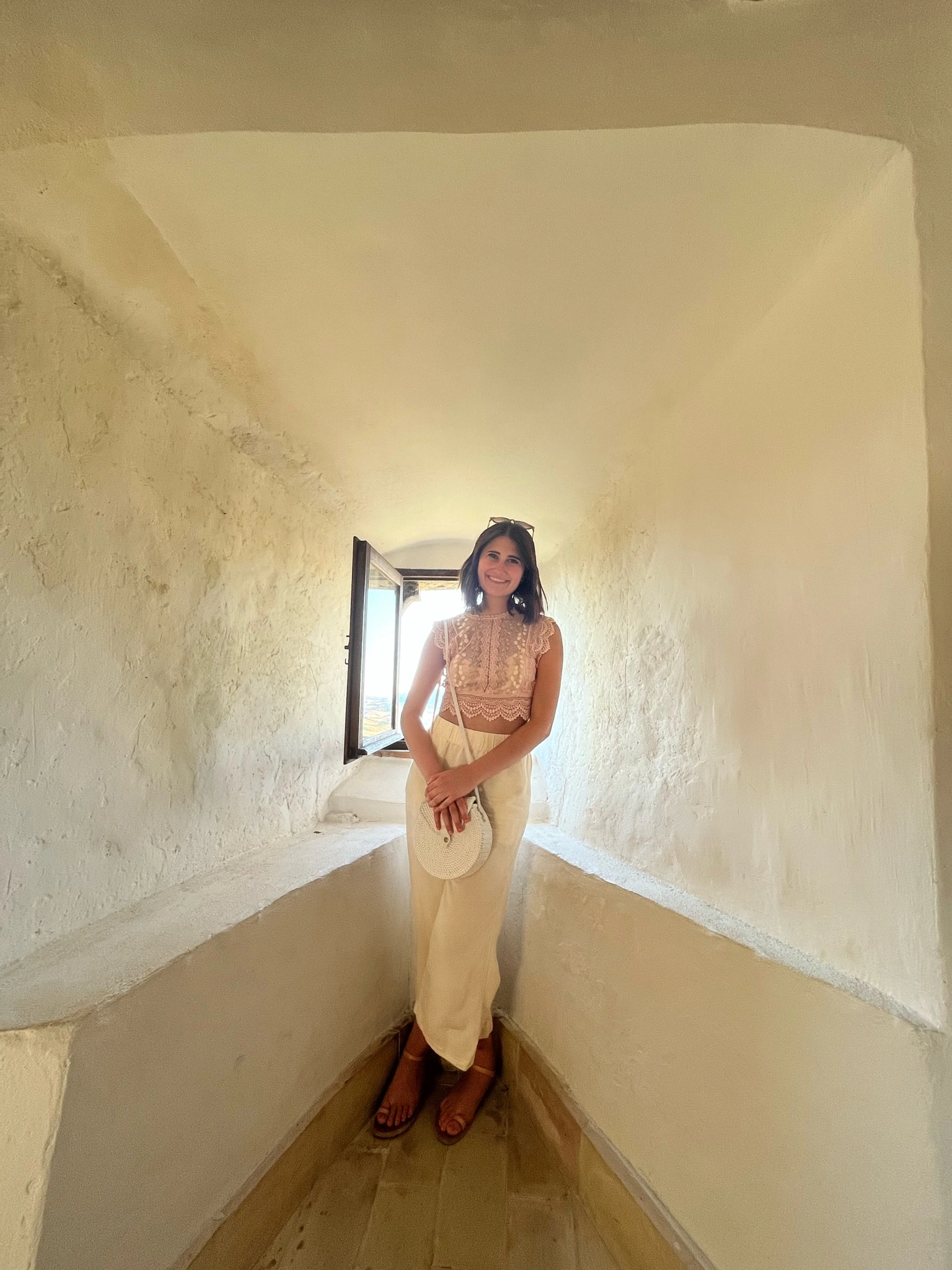 Violetta standing beside an open window in a pale stone alcove in Italy